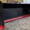 A red and black plow is on the ground.