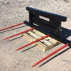 A black metal frame with six red prongs resting on a wooden pallet outdoors.