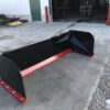 A red and black plow sitting in the middle of a driveway.