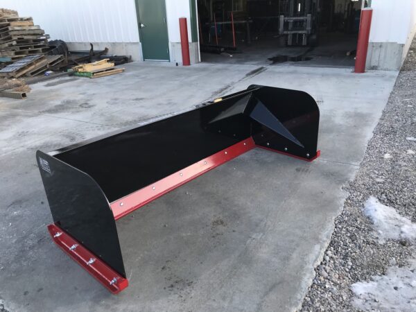 A red and black plow sitting in the middle of a driveway.