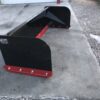 A black and red plow is sitting on the cement.
