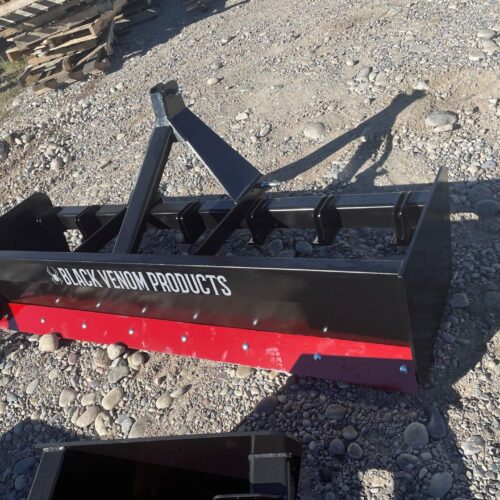A black and red plow is sitting on the ground.