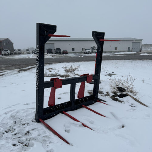 A tractor mounted hay bale handler in the snow.