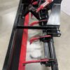 Close-up of a red and black snow plow attachment on a concrete floor.