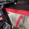 Close-up of black and red metal machinery parts with bolts and a hook.