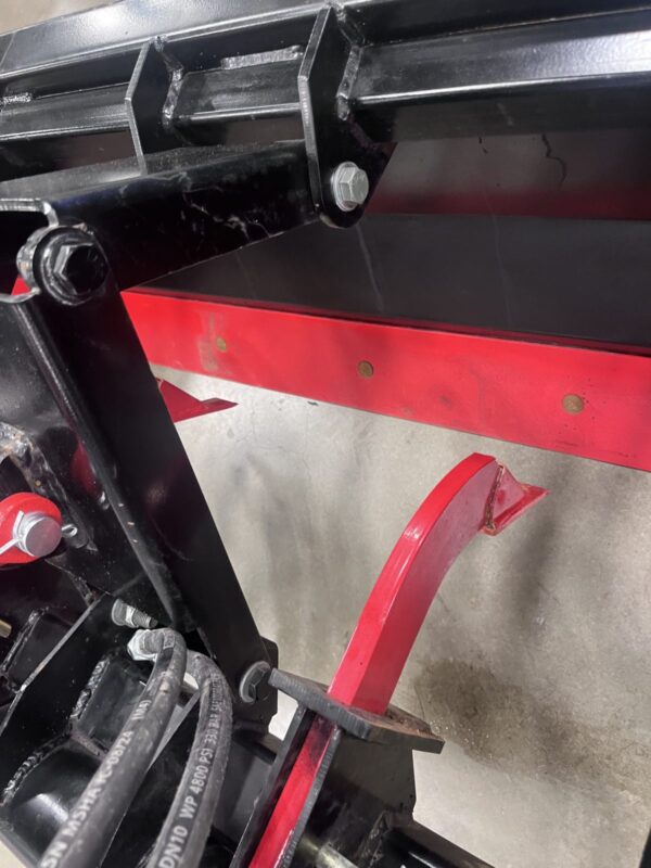 Close-up of black and red metal machinery parts with bolts and a hook.