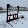 A forklift attachment with red prongs on snow-covered ground.