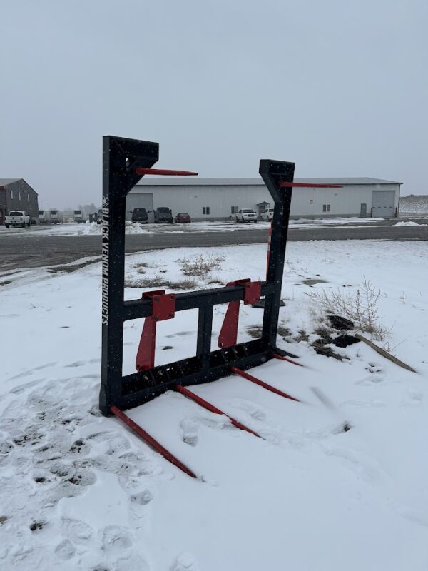 A forklift attachment with red prongs on snow-covered ground.