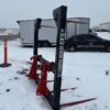 Snow-covered farm equipment with a black vehicle and trailer in the background.