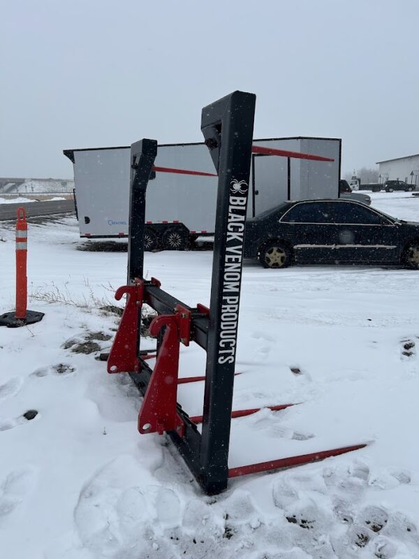 Snow-covered farm equipment with a black vehicle and trailer in the background.