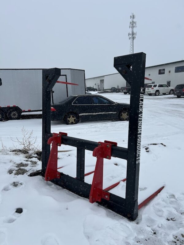 Heavy-duty metal frame with red clamps on snowy ground near trucks.