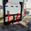 A forklift attachment with red prongs and black frame outdoors.