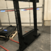 A black squat rack in a gym setting with a barbell and weights.