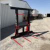 Red forklift attachment with four prongs outdoors near storage units.