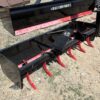 A red and black agricultural rotary tiller attachment on dry soil.