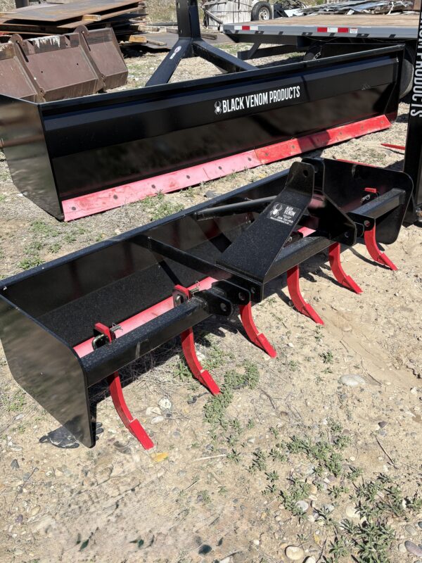 A red and black agricultural rotary tiller attachment on dry soil.