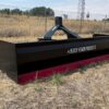 A large black and red land leveler on dry grass.