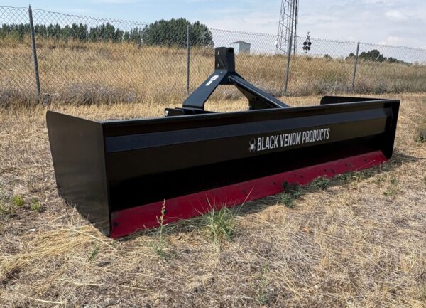 A large black and red land leveler on dry grass.