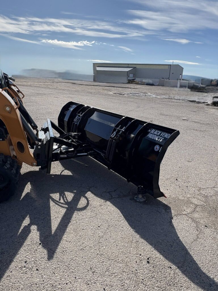 A yellow loader holding a large black snow plow attachment outdoors.