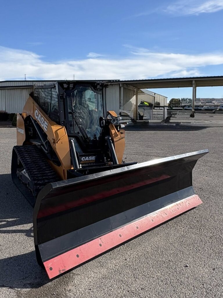 A skid steer with a snow plow attachment parked on asphalt.