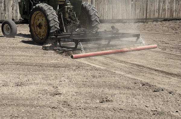 Tractor grading dirt field with attachment.